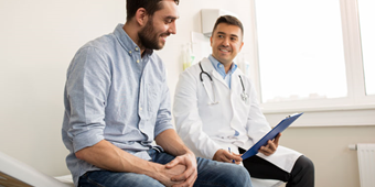A family doctor and male patient smile at each other as they discuss his health