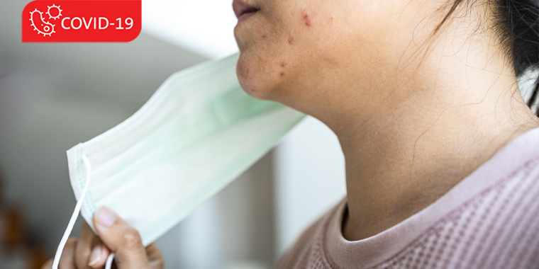 Woman with acne taking off her face mask