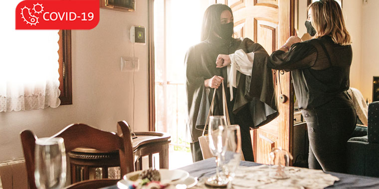 Two women wearing face masks touch elbows at a holiday gathering