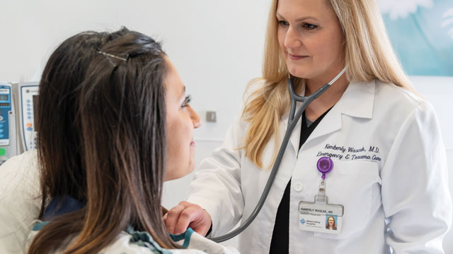 An emergency doctor, wearing a stethoscope, listens to a patient's heartbeat