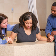 A woman during natural childbirth, in a birthing tub, assisted by a nurse and a man.