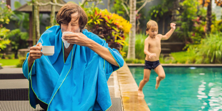 Man with an illness/cold sits next to a pool outside in the summer