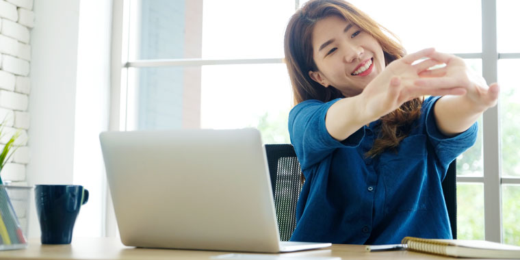 Woman stretches her arms as she sits at her work desk.