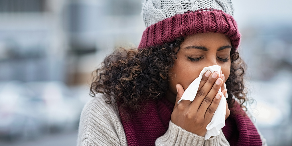 Women in sweater and winter hat sneezing