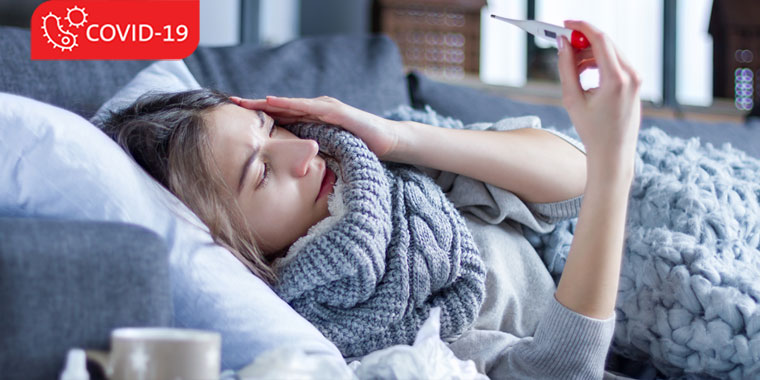 Women grasping the side of her head, while lying on the couch, and checking her temperature