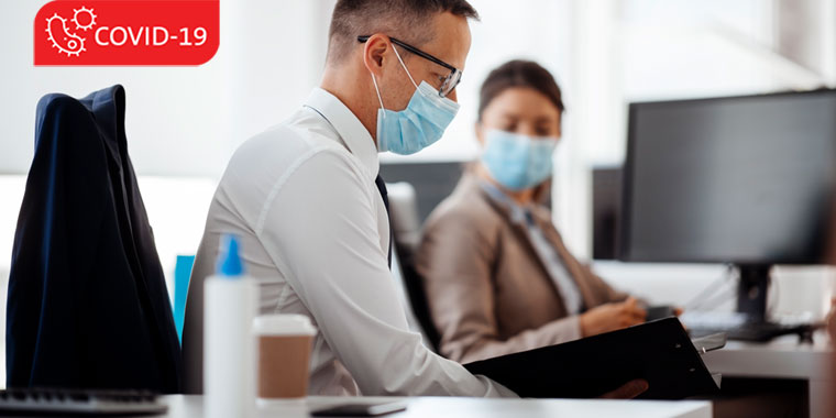 Male and female co-workers, in a work environment, wearing masks