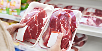 Person holding two packages of red meat